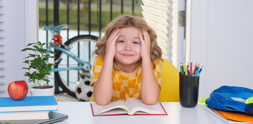 child sitting on a table with open book and hands in the face